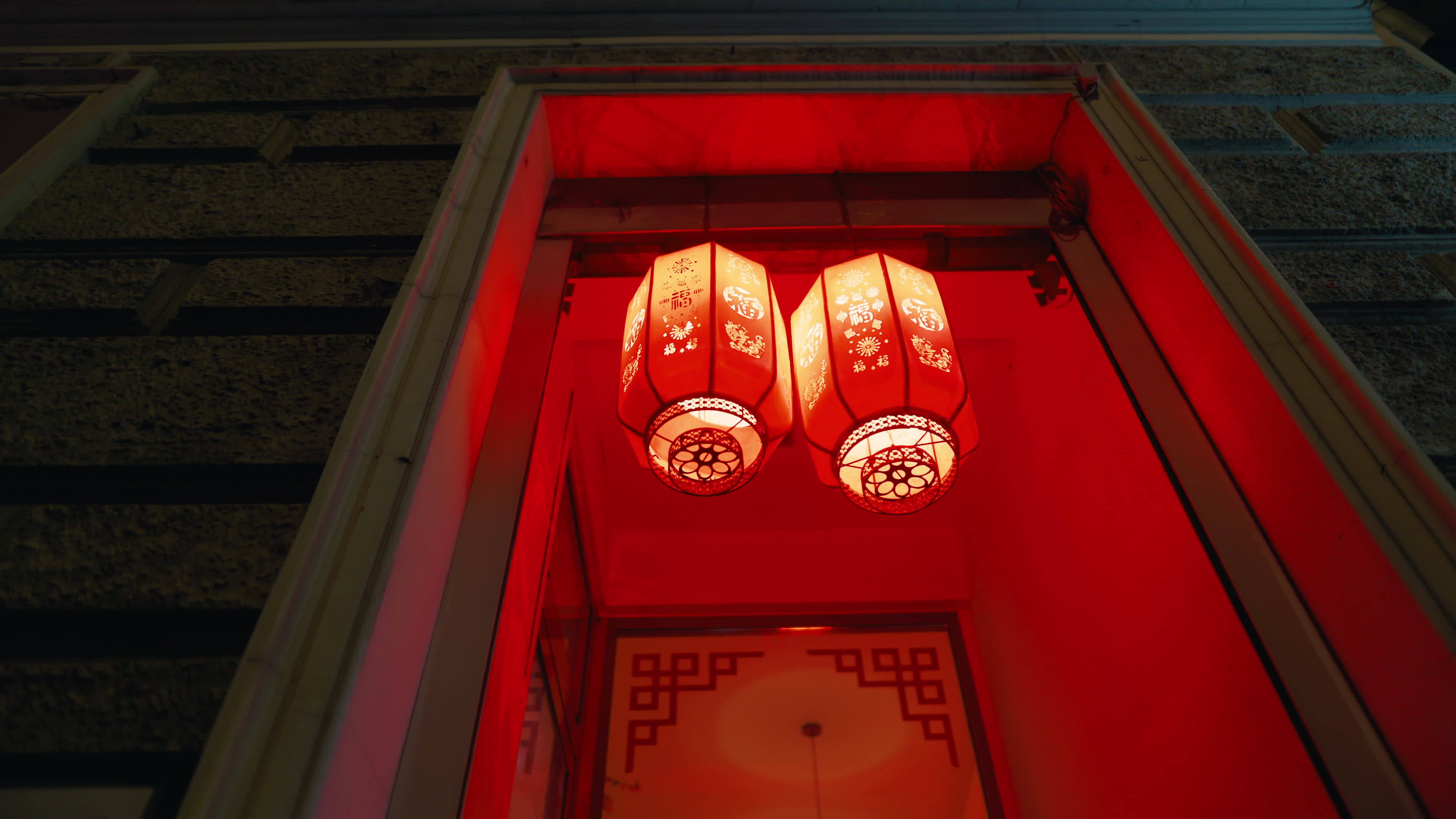 Two carmine red lanterns hang symmetrically from the ceiling in a dark