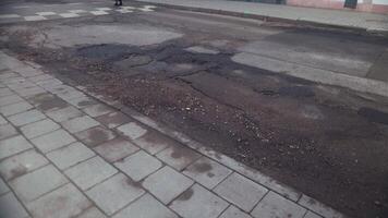Person navigating uneven road surface with numerous potholes on narrow street video