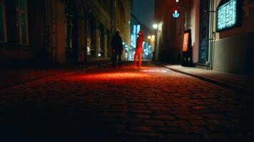 Two figures stroll down dimly lit cobblestone street at night video