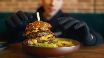 hombre con negro guantes complacer en rápido alimento, disfrutando un hamburguesa y papas fritas video