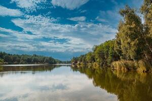 Beautiful view of the lake with blue sky, clouds, and green trees photo