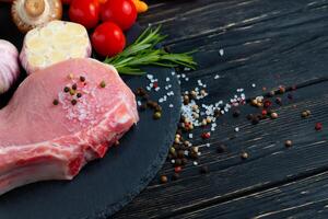 Top view of one pieces raw pork chop steaks with on a black stone cutting board. photo