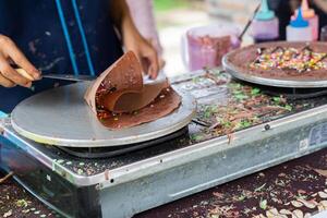 haciendo de crepes panqueques con chocolate y chocolate arroz en abierto mercado festival justo. un mano es haciendo crepes al aire libre en un metal plancha foto