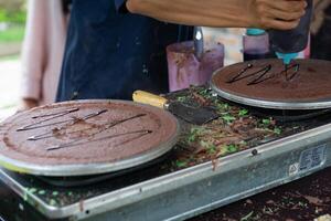 haciendo de crepes panqueques con chocolate y chocolate arroz en abierto mercado festival justo. un mano es haciendo crepes al aire libre en un metal plancha foto