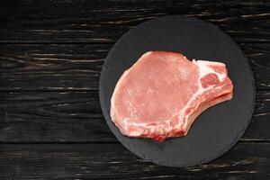 Top view of one pieces raw pork chop steaks on a black stone cutting board. photo