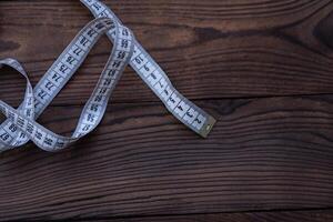 White measuring tape of a tailor lies in corner on dark wooden background. photo