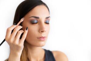 Make-up artist applying bright base color eyeshadow on model's eye and holding a shell with eyeshadow on background photo