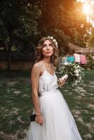 portrait of a beautiful young sexy girl bride with flowers in her hair look attractive in a white dress on a background of summer nature background posing and smiling photo