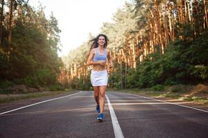 Beautiful caucasian young girl athlete runs sunny summer day on  asphalt road in the forest. photo