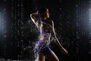 Beautiful athletic caucasian girl with a perfect figure is standing under the water. Fitness woman in a spray of water. Sports freshness. concept photo