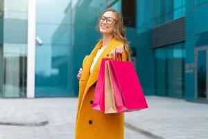 Business woman with shopping bags dressed yellow coat walking outdoors corporative building background photo