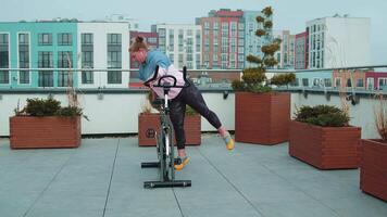 atletisk flicka göra akrobatisk lura på cykel utövar träna på stationär cykling maskin utomhus video