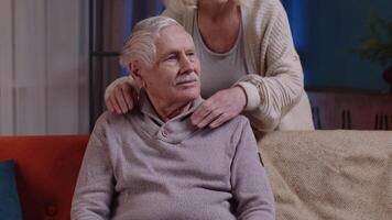 Happy old senior elderly family couple hugging, smiling, smiling looking at camera at home sofa video