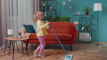 Child girl kid washes floors with a mop in domestic living room dancing, singing in positive mood video