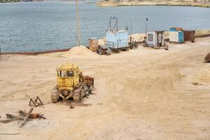 Sand quarry mining industry equipment excavator tractor standing sand land near lake water photo