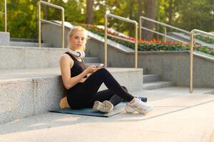 Sport and Fitness Young Adult Caucasian Woman Sitting Exercise Mat Concrete Floor Resting after morning Workout Outdoor Summer Park photo