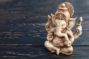 Hindu god Ganesh on black background. Statue on wooden table photo