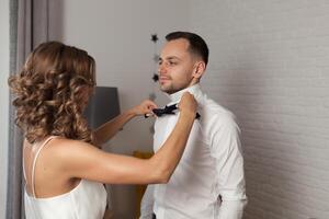 novia arregla arco Corbata en novio s cuello mientras ellos estar foto