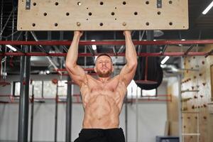 Man climbing pegboard gym athlete training arm strength stamina alpinism indoor. Ideal body with perfect abs naked torso photo