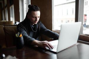 joven empresario con rastas teniendo haciendo su trabajo en café con ordenador portátil. foto