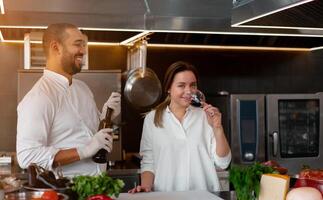 Handsome young African chef is cooking together with his Caucasian girlfriend in the kitchen using red wine as an ingredient. photo