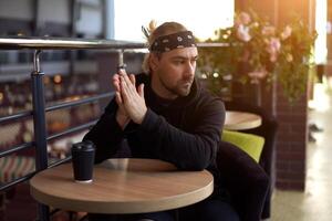 Young handsome lonely man sits cafe table sad waiting for meeting drinking coffee from a paper cup. photo