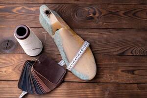 Leather samples for shoes and wooden shoe last on dark wooden table. photo