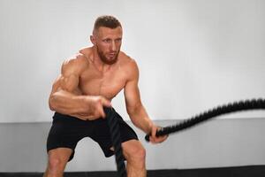 Gym battle rope man stamina training Athlete guy fitness exercising endurance indoor workout. photo