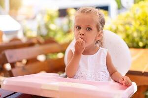 linda pequeño caucásico niña comiendo espaguetis a mesa sentado en niño asiento al aire libre restaurante. foto