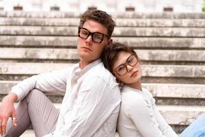 Young beautiful hipster couple in sunglasses in love sitting stairs on old city street photo