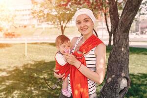 Mother carry a infant baby in wrap sling in park. Springtime. Concept of natural parenting photo