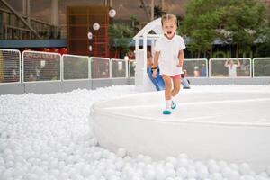 Happy little girl playing white plastic balls pool in amusement park. playground for kids. photo