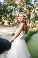 Follow me my love concept. Attractive young woman dressed in white wedding dress holding hand of her boyfriend and walking on the beautiful garden to happy future photo