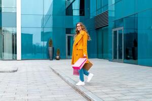 Business woman with shopping bags dressed yellow coat walking outdoors corporative building background photo
