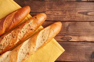 Three crispy french baguettes lie on an old wooden table with free space for text photo