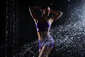 hermosa atlético caucásico niña con un Perfecto figura es en pie debajo el agua. aptitud mujer en un rociar de agua. Deportes frescura foto