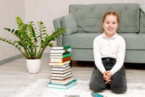 smiling girl sitting on the floor next to a stack of books at home photo