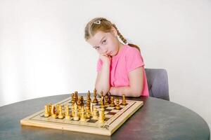 pensativo niña se sienta en frente de el tablero de ajedrez y piensa acerca de el siguiente moverse foto