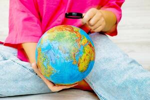 a woman examines the globe she holds in her hands with a magnifying glass photo