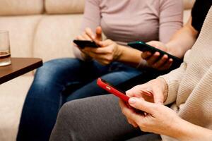 women sitting on the sofa and looking at their phones photo