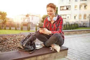 portrait of a young redhead female student in a checkered shirt. The girl listens to music in headphones. photo