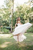 joven niña en un blanco vestir en el prado. mujer en un hermosa largo vestir posando en el jardín. maravilloso novia en un Boda vestir foto