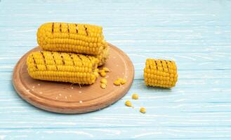 Grilled hot Corn cob lies on cutting board blue wooden table background. photo