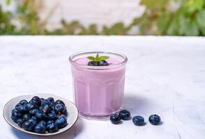 Tasty fresh blueberry yoghurt shake dessert in glass standing on white table background. photo