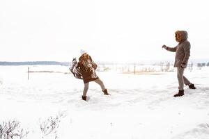 despreocupado contento joven Pareja teniendo divertido juntos en nieve en invierno bosque lanzamiento bolas de nieve a cada otro durante un burlarse de lucha foto