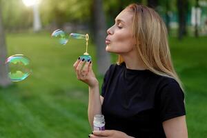 Young beautiful girl inflates soap bubbles in the summer sunny park photo