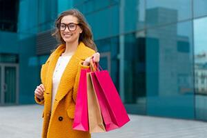 Business woman with shopping bags dressed yellow coat walking outdoors corporative building background photo