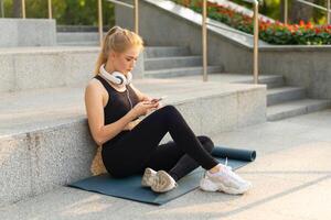 Sport and Fitness Young Adult Caucasian Woman Sitting Exercise Mat Concrete Floor Resting after morning Workout Outdoor Summer Park photo