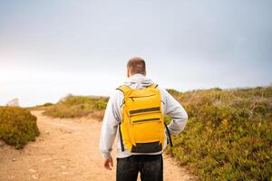 Rear-view young man traveler with yellow backpack photo