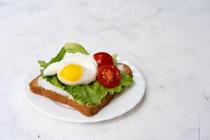 Sandwich with fried eggs salad and tomato on a white plate on a white background. photo